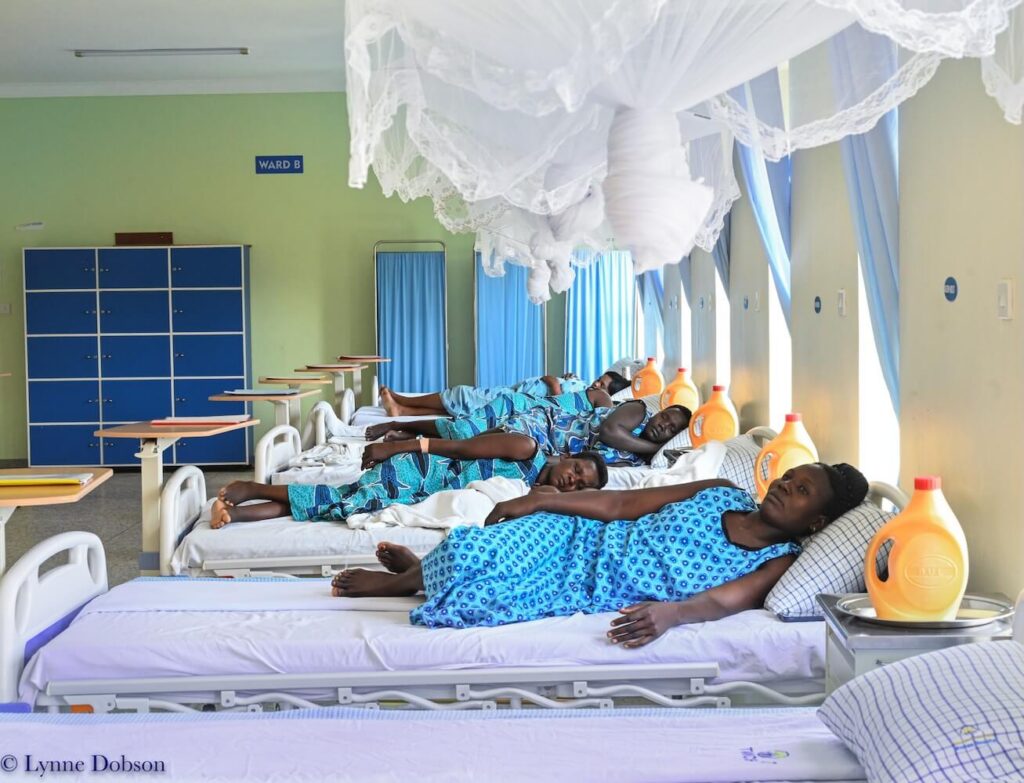 Women recovering in hospital beds at Terrewode Women's Community Hospital in Uganda, beneath white mosquito nets.